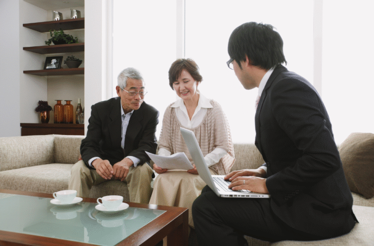Financial advisor meeting with an elderly couple at home, discussing estate planning documents over coffee in a relaxed and professional setting.